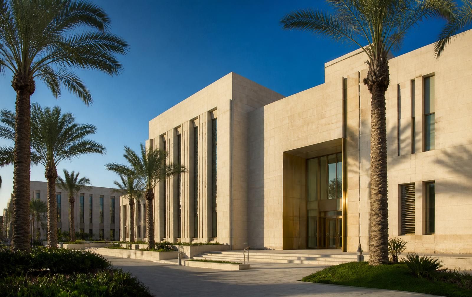 The Lighthouse Campus building in Mohandessin, Giza — a modern limestone institutional facade framed by mature palm trees under a deep blue sky